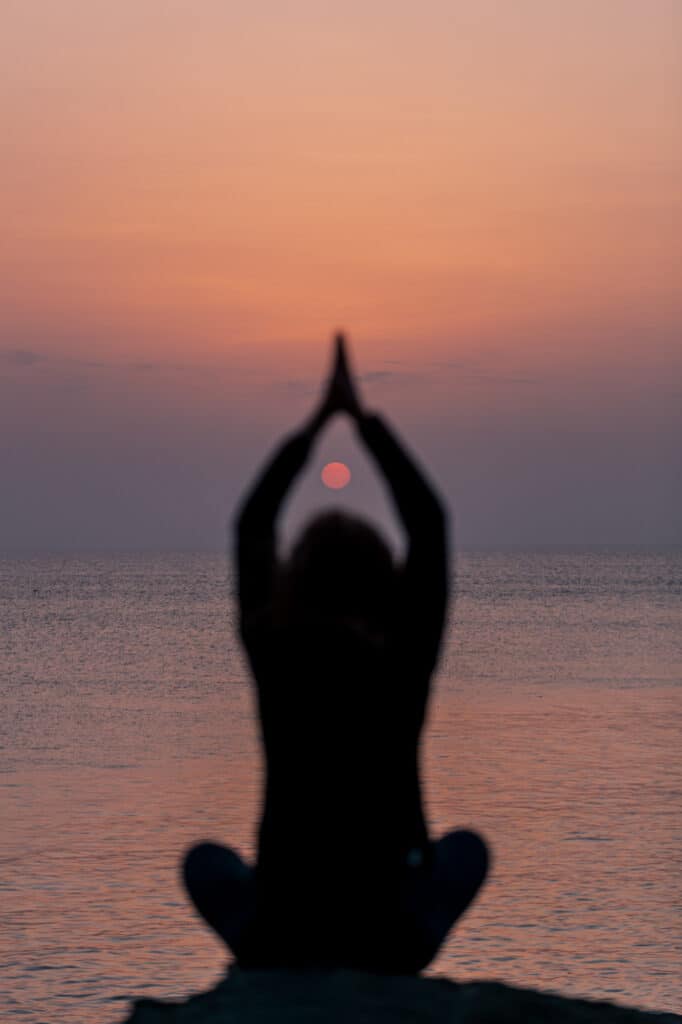 Silhouette en posture de yoga au coucher du soleil face à l'océan sur la côte d'Anglet