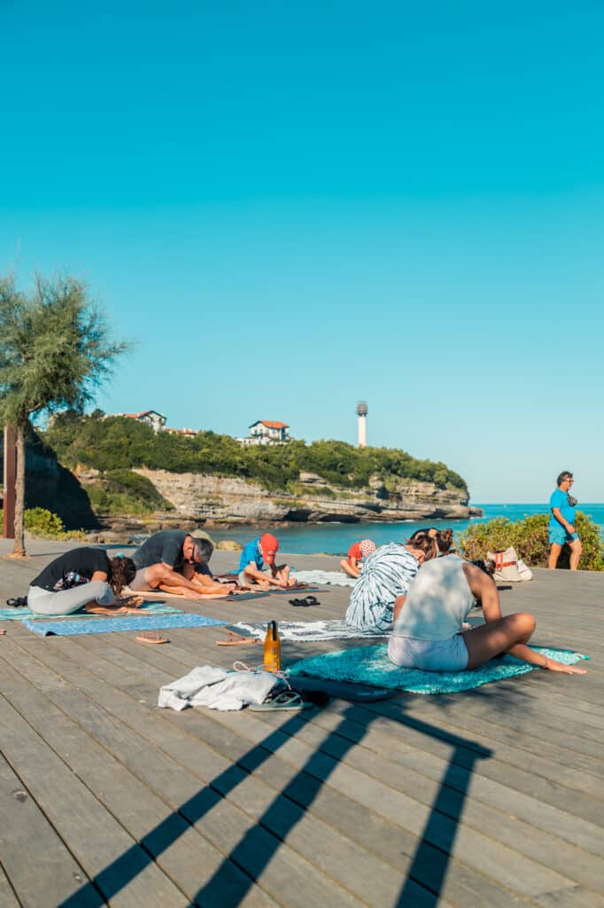 Groupe pratiquant le yoga en plein air face à l'océan sur le deck de la Chambre d'Amour à Anglet